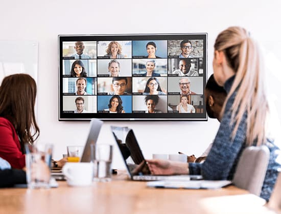 Staff in a meeting room looking at a display with a video conference in progress